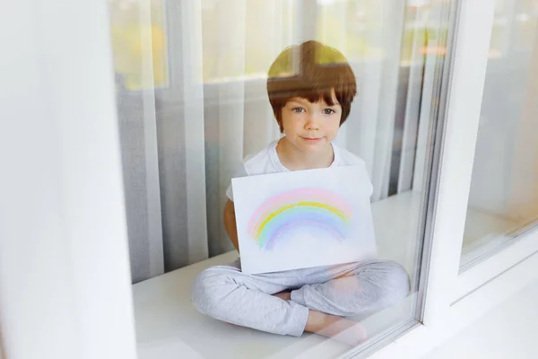 自宅でCovid 19隔離中の子供の絵虹 窓の近くの少年 家にいる コロナウイルスの予防のためのソーシャルメディアキャンペーン コロナウイルスのパンデミックの概念の間の希望 — ストック写真