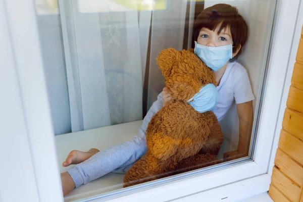 可怜的小男孩抱着一只泰迪熊 看着窗外 呆在家里 了解社交媒体活动和预防考拉病毒 — 图库照片