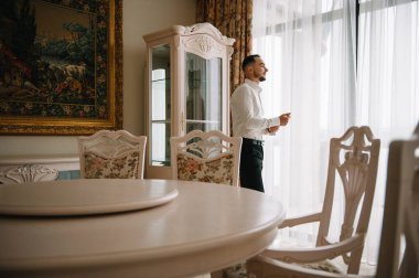 Saygıdeğer genç bir adam klasik iç mimarisi olan bir odada duruyor. Lüks. Erkek güzelliği, moda.