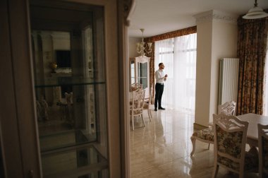 Saygıdeğer genç bir adam klasik iç mimarisi olan bir odada duruyor. Lüks. Erkek güzelliği, moda.