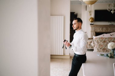 Ciddi bir adam iyimser bir havada gömleğini ilikliyor, işe hazırlanıyor.