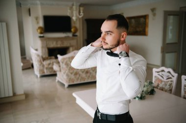 Ciddi bir adam iyimser bir havada gömleğini ilikliyor, işe hazırlanıyor.