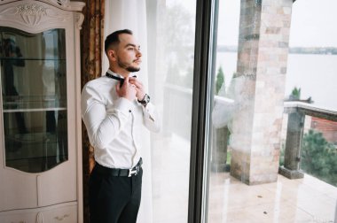 Ciddi bir adam iyimser bir havada gömleğini ilikliyor, işe hazırlanıyor.