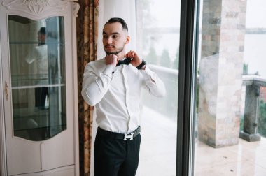 Ciddi bir adam iyimser bir havada gömleğini ilikliyor, işe hazırlanıyor.