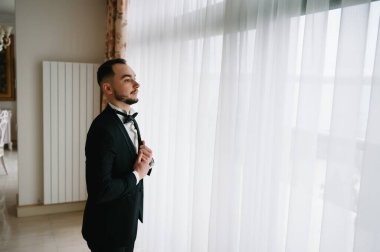 Saygıdeğer genç bir adam klasik iç mimarisi olan bir odada duruyor. Lüks. Erkek güzelliği, moda.