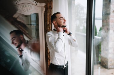 Ciddi bir adam iyimser bir havada gömleğini ilikliyor, işe hazırlanıyor.