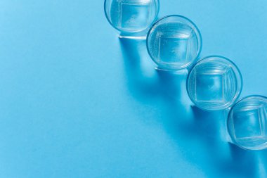 Bardaklar, su dolu bir bardak, açık mavi arka planda. Farklılık konsepti. Eşitlik kavramı.