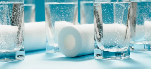 Bardaklar dolusu kirli ve berrak su ve evcil su arıtma sistemlerine açık mavi arka planda filtre kartuşları. Su arıtma kavramı.