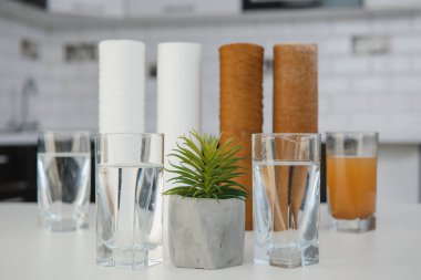 Kullanılan su filtresi kartuşu ve bir bardak paslı su kahverengi boya ve yeni filtre ve bir bardak temiz su. Musluk suyunun demir parçalarıyla kirlendiğine dair kanıt. beyaz mutfak