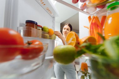 Sağlıklı yiyecek, sebze ve meyvelerle dolu açık buzdolabının yanında duran kadın portresi.