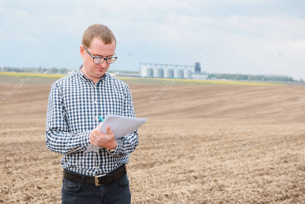 modern farmer checking his field plant and working on laptop computer against corn dryer silos in concept of industrial and agriculture