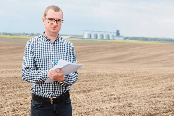 modern farmer checking his field plant against corn dryer silos in concept of industrial and agriculture