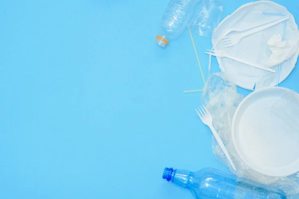 White single-use plastic and other plastic items on a blue background. The concept of choice without plastic or environmental problems.