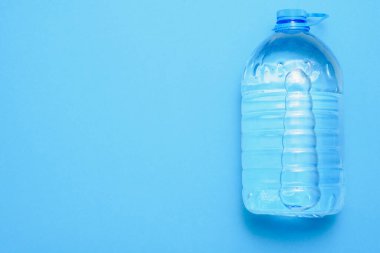 Temiz içme suyu olan büyük şeffaf plastik bir şişe. Mavi arkaplanda polipropilen kabın içindeki su.
