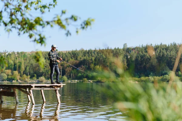 パイク パーチ 鯉の釣り ロッドを持つ漁師 川の岸にリールを回転させます 湖で釣りをしながらロッドを引いて魚を捕まえる男は テキスト空間で池 野生の自然 農村部の休暇の概念 — ストック写真