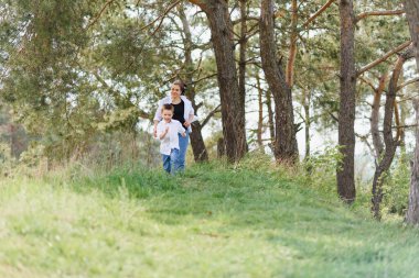 Anne ve küçük oğlu mutlu bir aile. Çekici anne, çocuk yazın dışarıda kaygısız yürüyor. Ebeveyn kadın bebekle birlikte doğaya gider, yaz, bahar günü. Işık, fotokopi alanı. Mutlu aile.