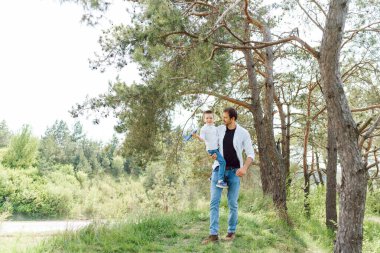 Yakışıklı baba ve küçük tatlı oğlu yeşil çimenlikte eğleniyor ve oynuyorlar. Mutlu aile kavramı. Aile hayatı olan güzel doğa manzarası. Aile birlikte dinleniyor. Babalar Günü