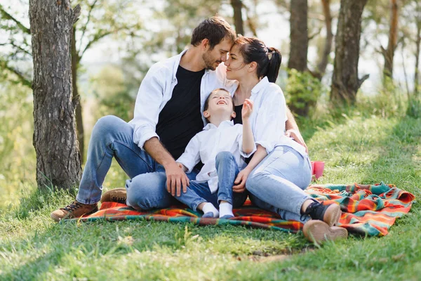 Mutlu bir genç aile yaz günü dışarıda yeşil çimlerin üzerinde otururken doğadaki güzel parkta eğleniyor. Mutlu aile.