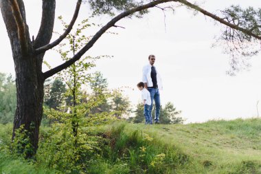 Yakışıklı baba ve küçük tatlı oğlu yeşil çimenlikte eğleniyor ve oynuyorlar. Mutlu aile kavramı. Aile hayatı olan güzel doğa manzarası. Aile birlikte dinleniyor. Babalar Günü