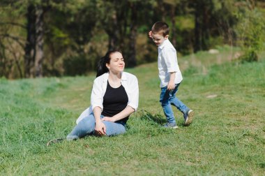 Mutlu aile! Anne ve oğlu çimenlerde birlikte oynuyorlar güneşli yaz gününde, hayat anında.