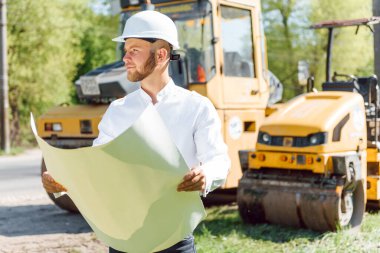 Yol makinelerinin yanında mühendis. Yeni bir asfalt yol yapma fikri. Yol tamiri. Pistin yakınında bir yol işçisi..