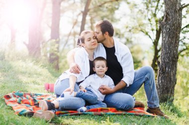 Mutlu anne, baba ve oğul parkta. Aile hayatı olan güzel doğa manzarası. Mutlu aile çimlerin üzerinde birlikte dinleniyor, dışarıda eğleniyor. Aile hayatında mutluluk ve uyum..