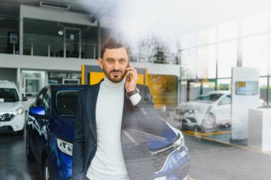 Gayri resmi kıyafet satan yakışıklı bir alıcı, çapraz kollu arabanın yanında dikilirken kameraya bakıyor.