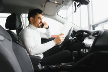 Güzel iş konuşması. Yakışıklı genç işadamı akıllı telefonuyla konuşuyor ve ön koltukta otururken gülümsüyor.