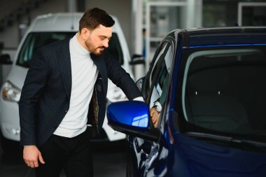 Yakışıklı bir adam gösteri odasında araba seçiyor.