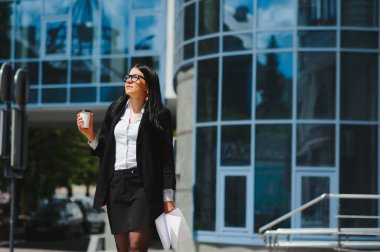 Ofis binasının yakınındaki kahve dükkanında güzel bir kadın işe gidiyor. Başarılı bir iş kadınının portresi. Şehir caddesinde işe giderken elinde sıcak bir bardak içki tutuyor. Yüksek Çözünürlük.