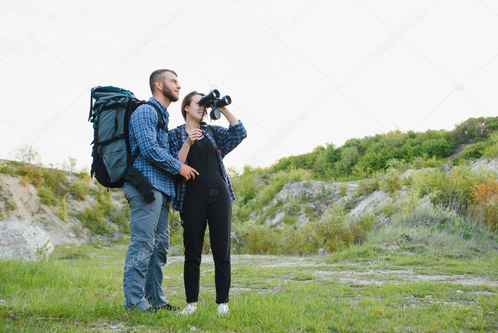 Couple enjoying beautiful views on the mountains, while traveling with backpacks in the mountains during the summer vacations