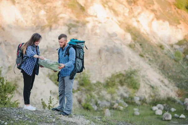 Couple of Young Happy Travelers Hiking with Backpacks on the Beautiful Rocky Trail at Warm Sunny Evening. Family Travel and Adventure Concept.