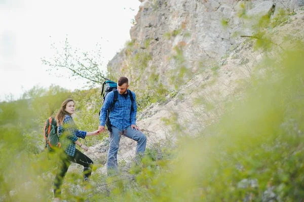 Hiker guy gives a hand to the girl while walking in the mountains, help and friendship concept