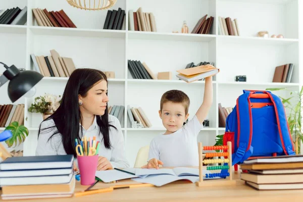 Female private tutor helping young student with homework at desk in bright child\'s room