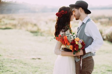 Gelin ve damat bir dağ deresinin arka planında. Şapkalı damat. Gelinin saçında çiçekler