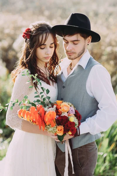 La novia y el novio en el fondo de un arroyo de montaña. el novio en el sombrero. flores en el pelo de la novia —  Fotos de Stock