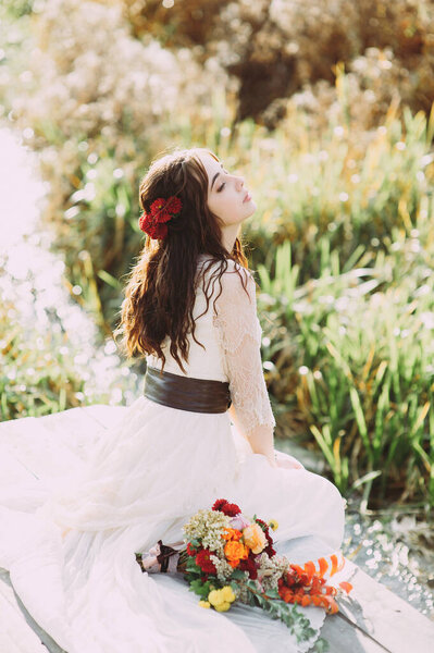 Beautiful young bride with flowers in her hair posing against the background of a river. bouquet and legs close-up