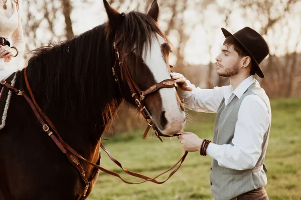 Όμορφος γαμπρός με καπέλο που χαϊδεύει άλογο. άντρας με άλογο. — Φωτογραφία Αρχείου