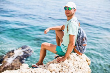 Genç adam sahilde otururken gülümseyen