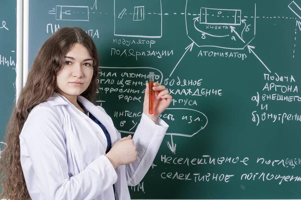 A student with a test tube in her hands is standing at the blackboard with chemical formulas. Fun time at the university.