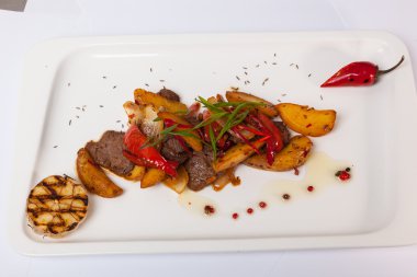 Beyaz tabakta patatesli baharatlı biftek.