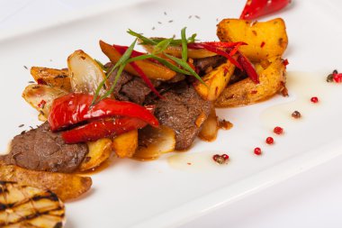 Beyaz tabakta patatesli baharatlı biftek.