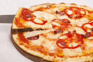 El küreği beyaz arka planda bir dilim pizza alır.
