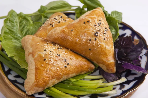 Oriental meat pies with greens on wooden plate