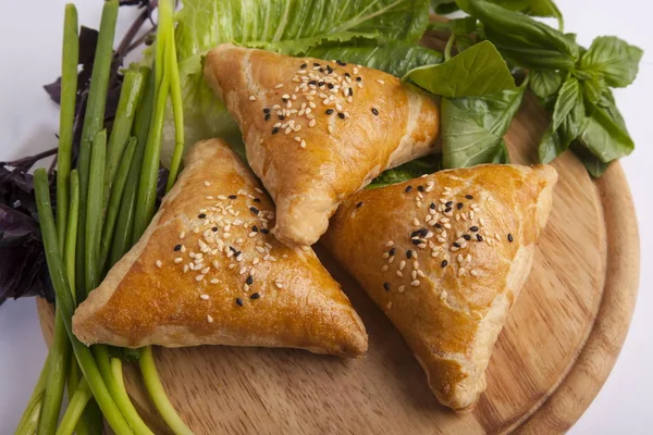 Oriental meat pies with greens on wooden plate