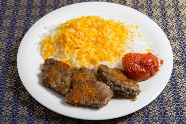 Beyaz tabakta pilavlı chelo kebabı.