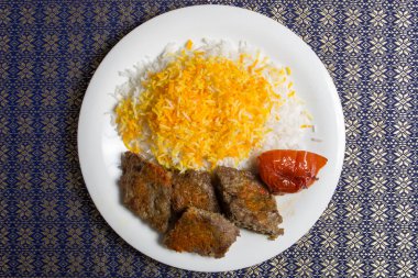 Beyaz tabakta pilavlı chelo kebabı.