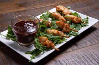 Beyaz dikdörtgen bir tabakta rucula soslu tavuk.