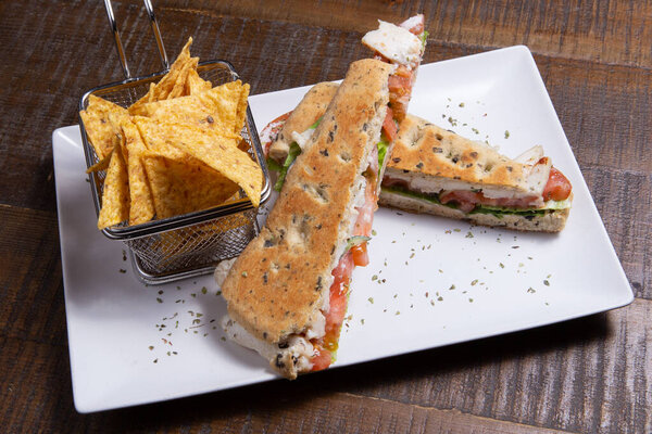 итальянский сэндвич с панини с курицей, помидорами и начос на белой тарелке
