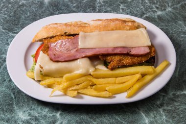 Beyaz mermer masada servis edilen tavuk, jambon ve pastırmalı lezzetli sandviç.